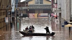 uma canoa em meio a rua alagada com pessoas remando